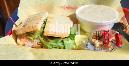 Basket, with yellow paper, holds a fresh crab sandwich and a bowl of clam chowder. Stock Photo
