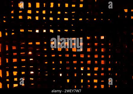 The light of a candle is visible through a fine straw mesh in the dark, background, mesh for background Stock Photo