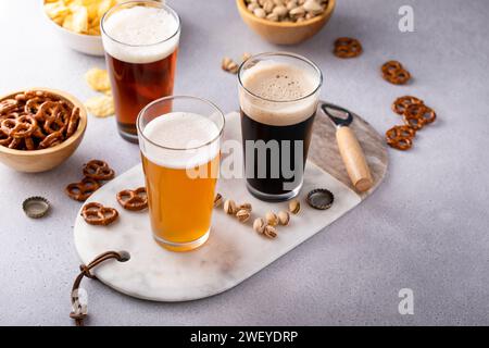 Dark stout, lager and ale beer in tall glasses on the table, variety of beer with snacks, pretzels and chips Stock Photo