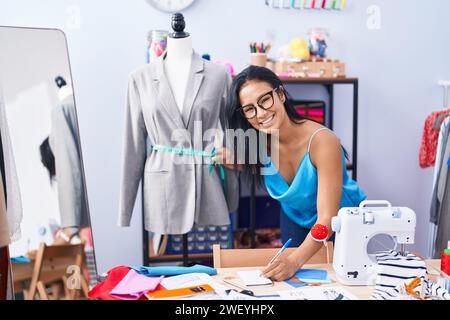Young beautiful latin woman tailor measuring jacket writing on notebook at florist Stock Photo