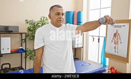 Hispanic mature man exercising with dumbbell in rehabilitation clinic interior Stock Photo