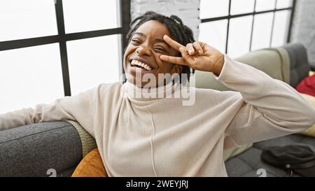 A joyful african american woman with dreadlocks posing playfully in a cozy living room setting. Stock Photo