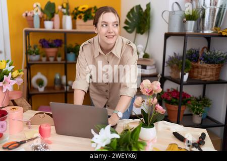Young caucasian woman florist smiling confident using laptop at flower shop Stock Photo