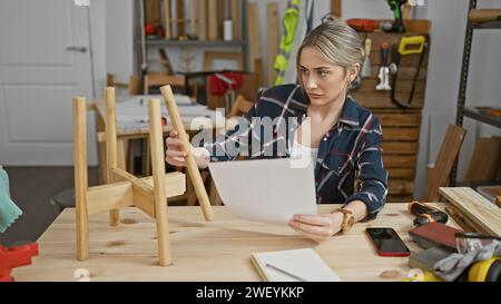 Caucasian woman reading plans in a woodworking workshop with tools and timber around Stock Photo