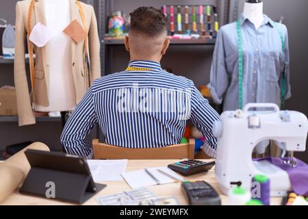 Hispanic man with beard dressmaker designer working at atelier standing backwards looking away with arms on body Stock Photo