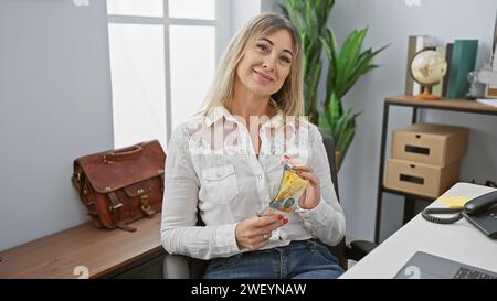 Caucasian woman holding swiss francs in modern office setting, conveying business and financial themes. Stock Photo