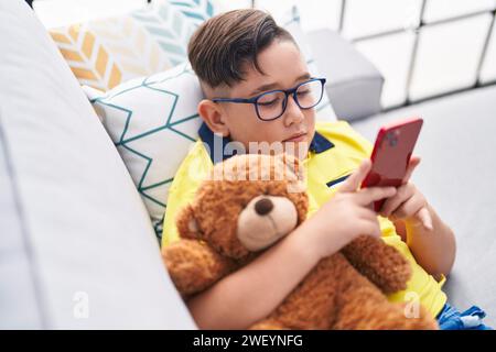 Adorable hispanic boy using smartphone hugging teddy bear at home Stock Photo