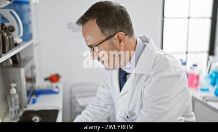 Concentrated middle-aged man with grey hair, immersed in groundbreaking science, harnesses computer power in the buzzing lab environment Stock Photo