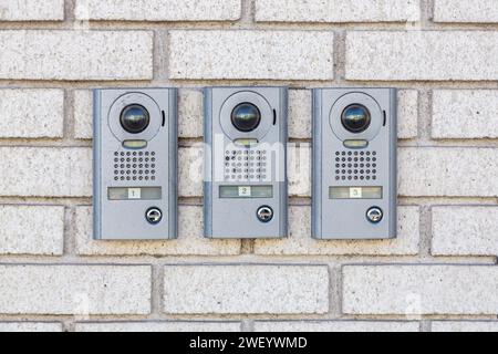 Three intercom on white textured brick wall, Close up. Apartment numbers and push button door buzzer. House intercom doorbell entrance home with a surveillance camera. Intercom doorbell on building Stock Photo