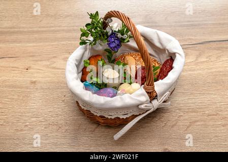 A wicker Easter basket filled with food standing on a table, decorated with boxwood and catkins. Stock Photo