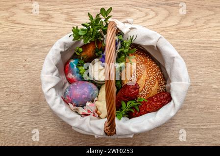 A wicker Easter basket filled with food standing on a table, decorated with boxwood and catkins. Stock Photo