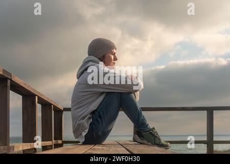 woman sitting on a bench looking out to sea, alone and thoughtful Stock Photo