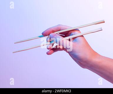 Hands holding Chinese sticks, food chopsticks, neon light Stock Photo