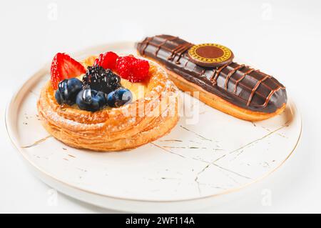 Delicious eclairs with berries and chocolate on a white plate. Stock Photo