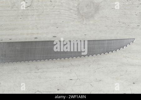 Details of Wavy Serrated Kitchen Knife on White Table Stock Photo