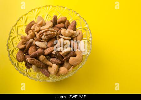 Salted mixed nuts in a glass bowl on a yellow background Stock Photo