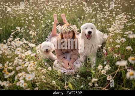 Woman dogs meadow chamomile. Woman embraces her furry friends in a serene chamomile field, surrounded by lush greenery. A heartwarming display of love Stock Photo