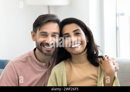 Happy attractive middle aged married couple hugging, sitting on couch Stock Photo