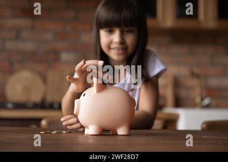 Little hispanic girl throwing coin to pink piggybank Stock Photo