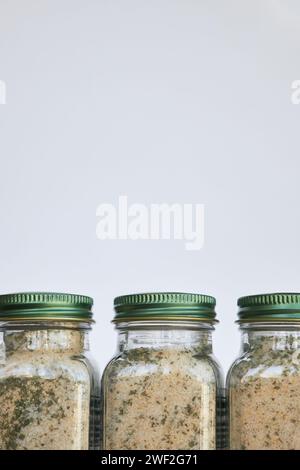 Packaging and storage of homemade seasoning. Three glass jars with green lid on gray background. Using reusable, recyclable. Aromatic Spices made from Stock Photo