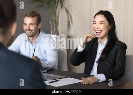 Happy cheerful diverse young colleagues laughing at meeting table Stock Photo