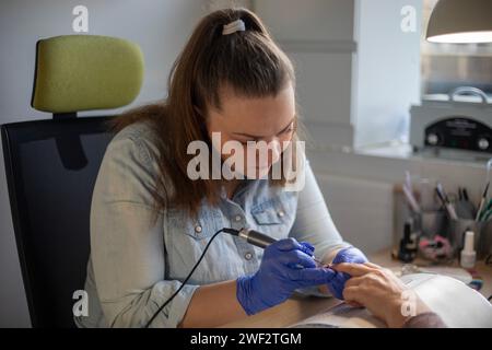 Close up of trained Nail technician focused on her work while filing her client's nail with an electric nail file. Senior Client getting a manicure Stock Photo