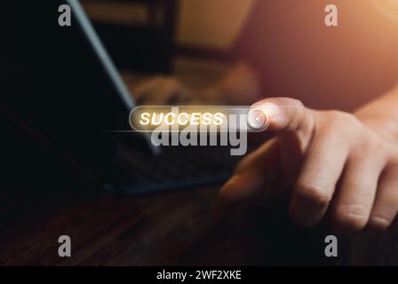 Word "SUCCESS" on virtual screen with 3d button or tab switch with target icon, pressing by person who working with laptop computer, dark background. Stock Photo