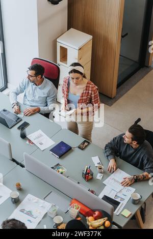 Overhead view of a different aged team engaging in a collaborative effort at a spacious office table, with computers, documents, and healthy snacks. Stock Photo