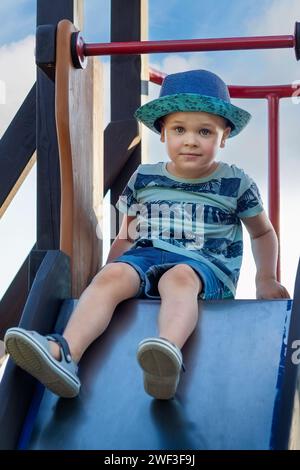 Happy kid boy having fun and climbing on outdoor playground. Funny child smiling and romping on slide. Summer and spring leisure for active kids. Boy Stock Photo