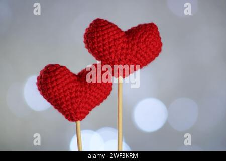 Two knitted red heart on gray background. Bright lights of night in the background. Valentine day concept idea. Selective focus. Abstract background. Stock Photo