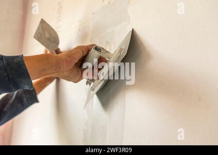 old manual worker with wall plastering tools renovating house. Plasterer renovating indoor walls and ceilings with float and plaster. Stock Photo