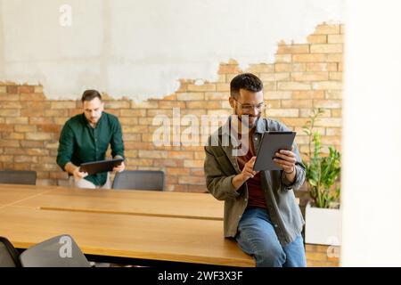 In a contemporary office setting, two focused colleagues engage in their work with tablet and laptop, collaborating and sharing ideas in a bright and Stock Photo
