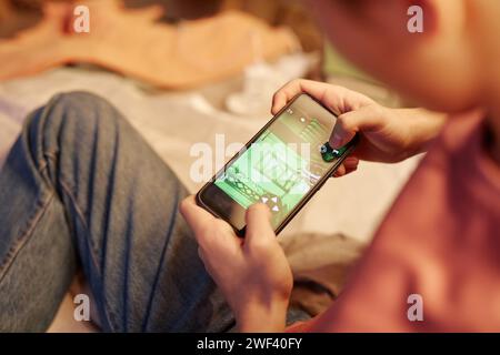 High angle closeup of teen boy holding smartphone and playing online mobile game with focus on screen Stock Photo