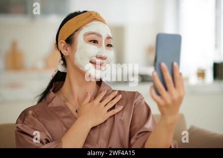 Portrait of smiling young woman with clay face mask on taking selfie Stock Photo
