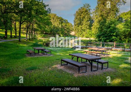 Wooden picnic tables near a river in Smiltene Old Park. Latvia. Recreational, picnic rest area in a park. Stock Photo