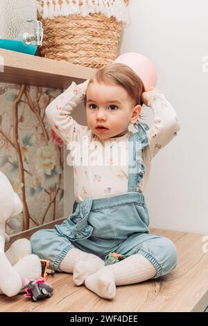 Little baby girl sitting on the table putting paper bucket on her head. Stock Photo