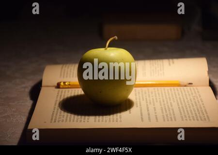 A stack of books in red covers and a red apple against the morning window. A metaphorical image of a good start to the day and life. Stock Photo