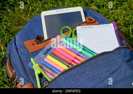 blue backpack with school supplies on the grass Stock Photo