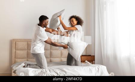 African American spouses having pillow battle for fun at bedroom Stock Photo