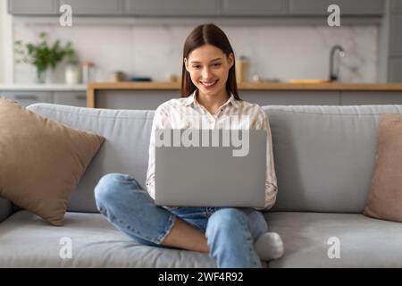 Happy woman using laptop on cozy sofa at home Stock Photo