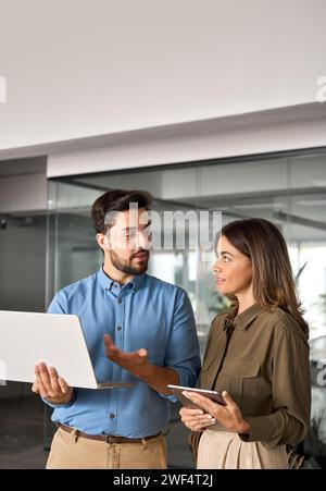 Busy professional employees working in office with laptop and talking, vertical. Stock Photo