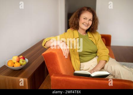 Happy senior woman reading book while relaxing on couch at home Stock Photo