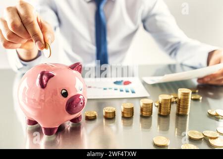 Banker accountant or insurer putting money in a piggy bank. Financial chart from coins business concept. Stock Photo