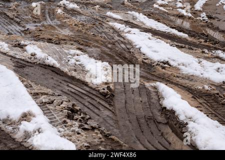 Patterns of car tire tracks weaving through the muddy, snow-laden road, highlighting the interaction between vehicles and the challenging winter terrain. Stock Photo