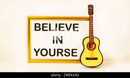 Golden frame with the text Believe in yourself, on a white background with a guitar Stock Photo