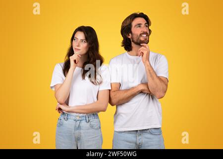 Thoughtful couple in white t-shirts, with the man and woman looking upwards with hand on chin Stock Photo