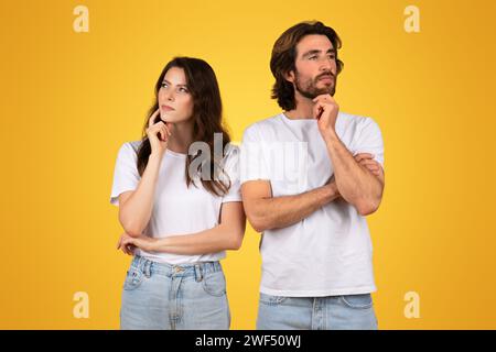 Pensive couple in white t-shirts and blue jeans, standing back-to-back with thoughtful expressions Stock Photo
