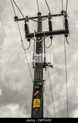A rural 11kV overhead line pole against an overcast sky, showing the coloured three phase identifiers and danger notice. County Durham, UK. Stock Photo