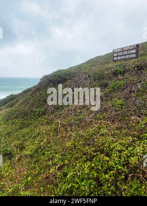 Wooden sign reading "Private Property - No Trespassing - No Beach Access" on a hillside near the ocean Stock Photo