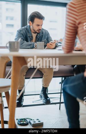 Focused man using smart phone in a casual office setting with colleagues Stock Photo